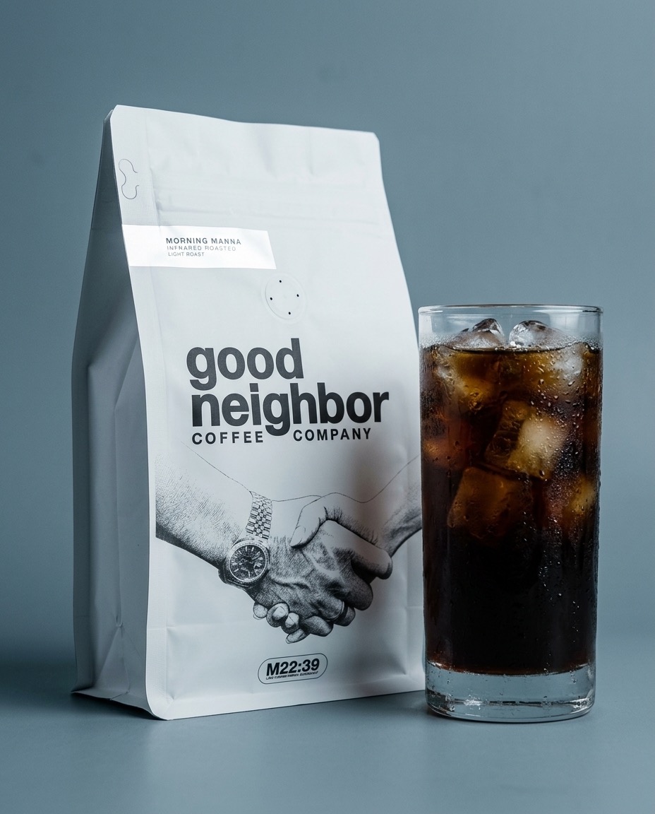 Good Neighbor Coffee Morning Manna bag beside a glass of iced coffee